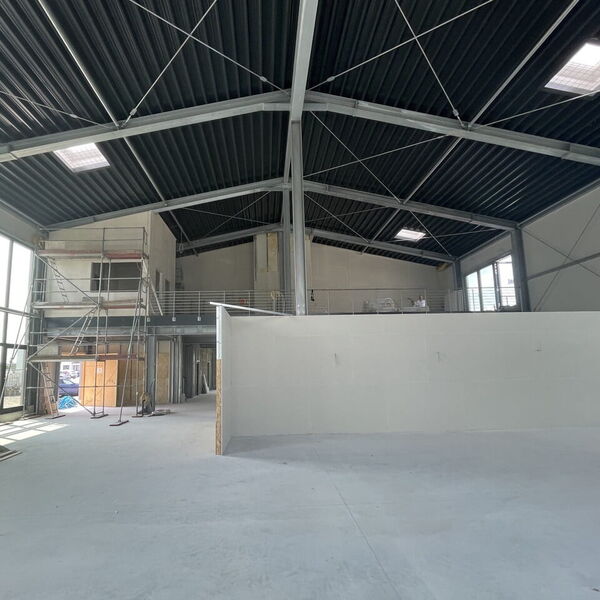 Innenansicht einer im Bau befindlichen Halle mit Stahlträgern, Trapezblechdach, Oberlichtern und Gerüsten