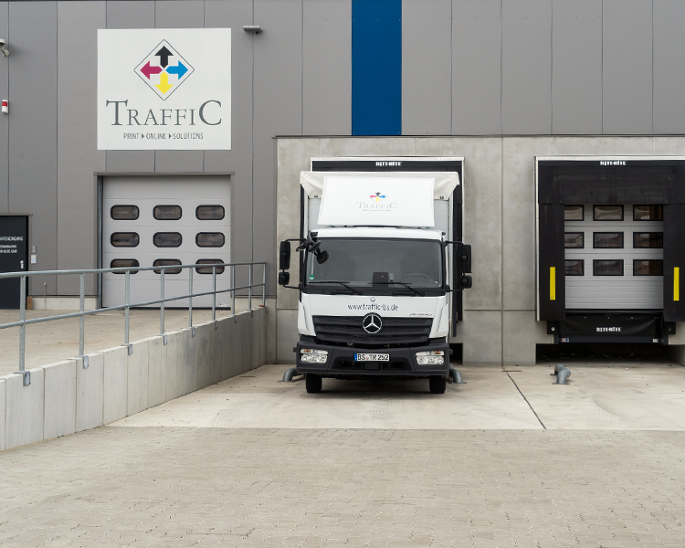 Ein weißer Lieferwagen mit dem Logo von TRAFFiC steht vor einem Industrietor