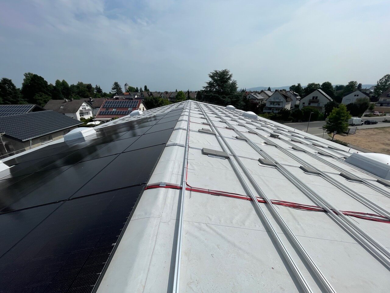 Dach mit Solarmodulen und Montageschienen, im Hintergrund Häuser und Bäume
